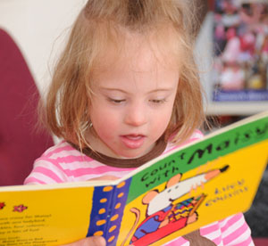 A toddler reading a "Count with Maisy" board book at the library.